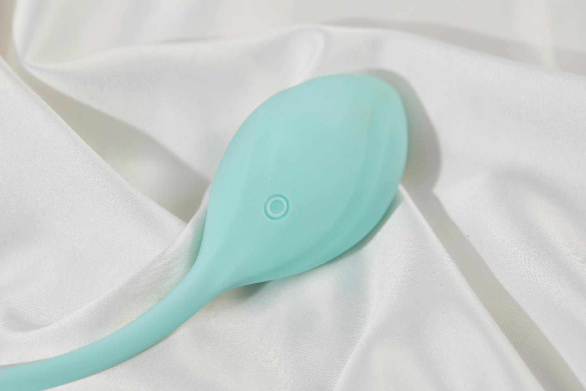 A teal clitoral vibrator on white silk fabric