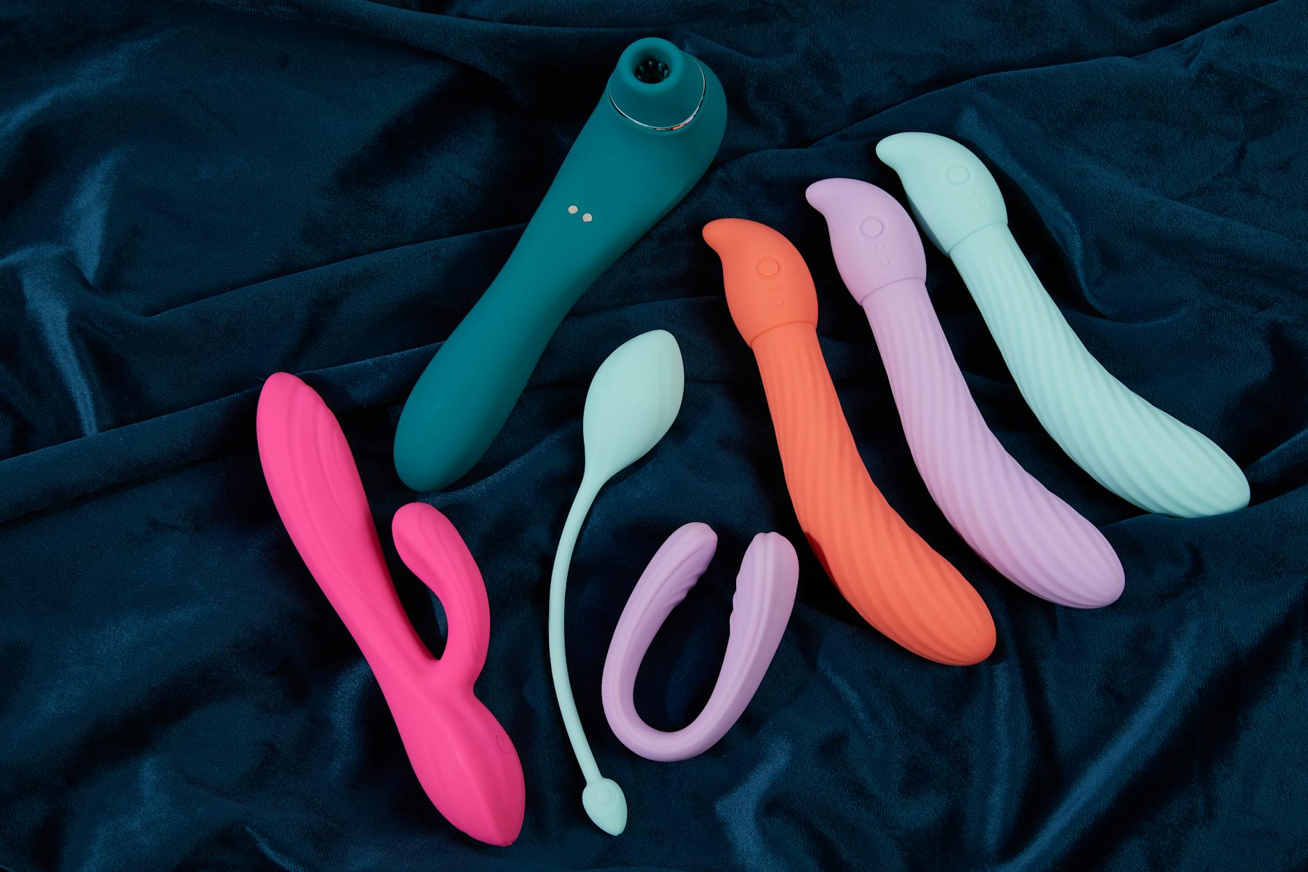 Collection of colorful silicone sex toys and vibrators displayed on dark blue fabric