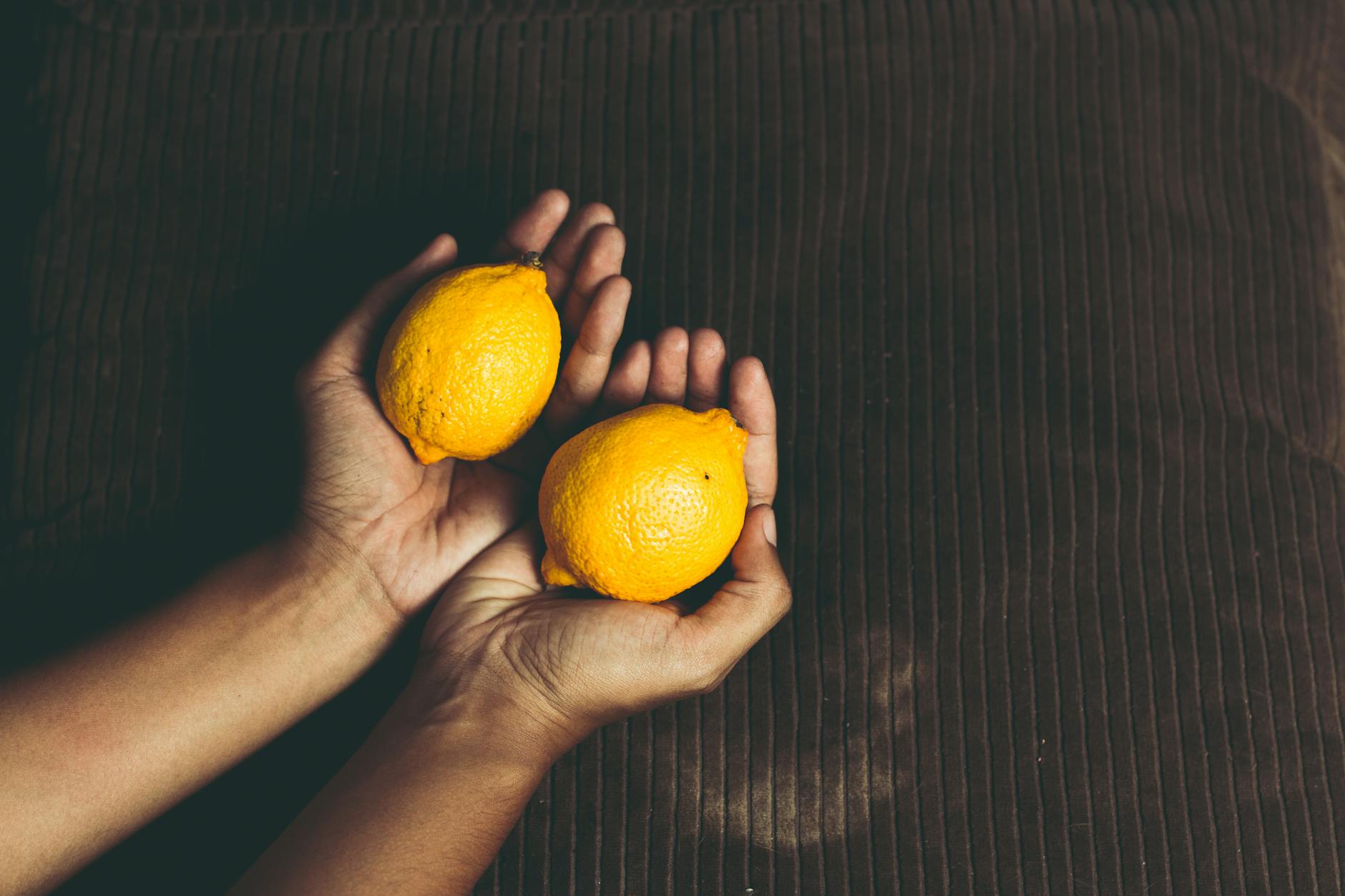 Close-up of a hand holding an orange vibrator against a minimalistic purple backdrop, showcasing modern sensuality