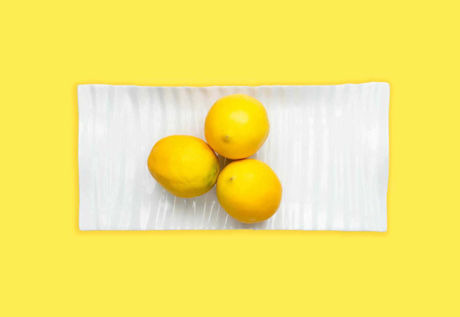 Fresh lemons on a white plate with yellow background, symbolizing reset and renewal