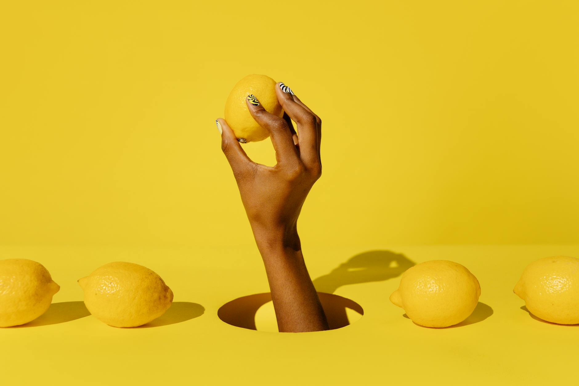 A hand holding a fresh lemon against a bright yellow background, symbolizing gentle citrus-inspired pleasure