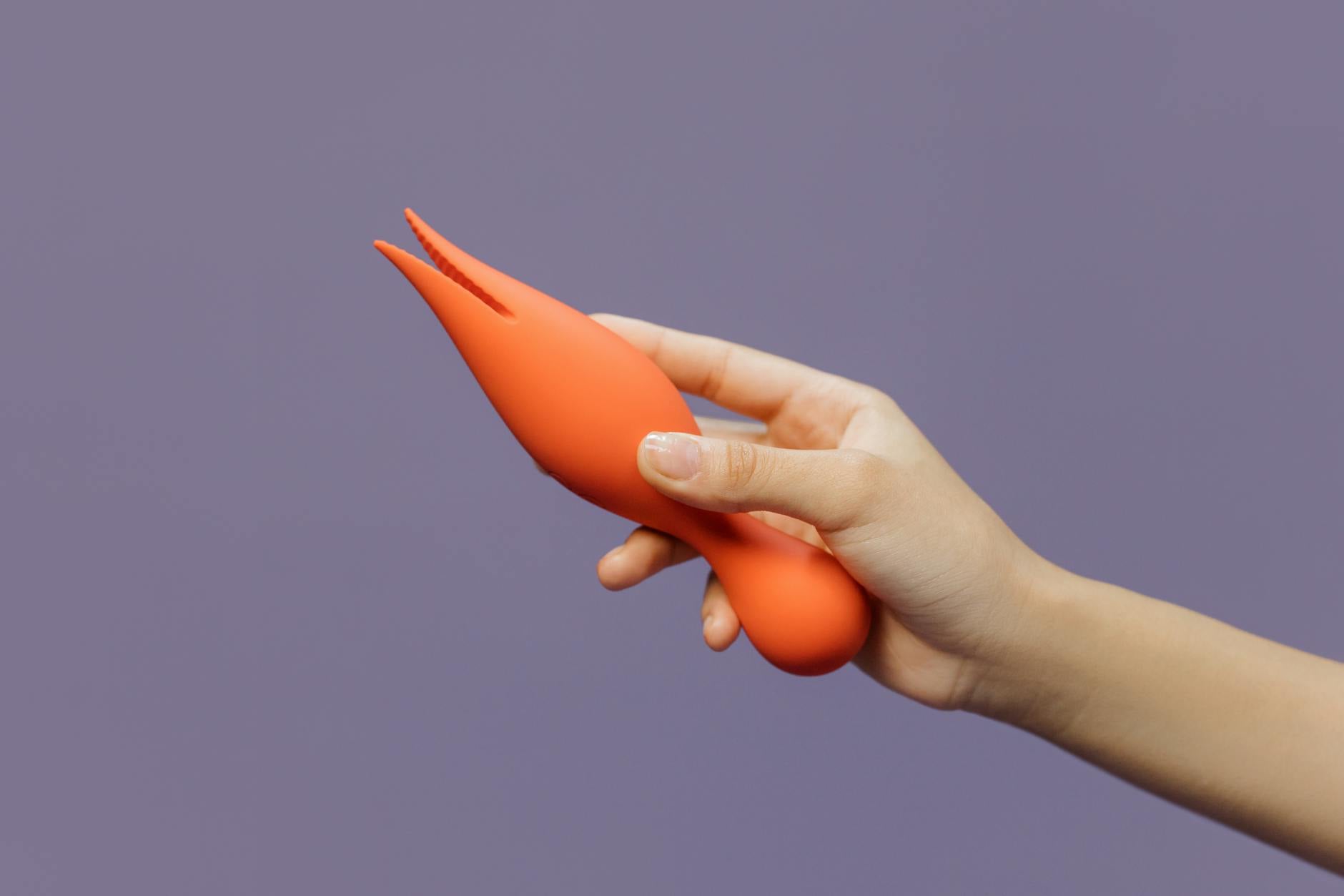 Hand holding a lemon clitoral vibrator against a minimalist purple background