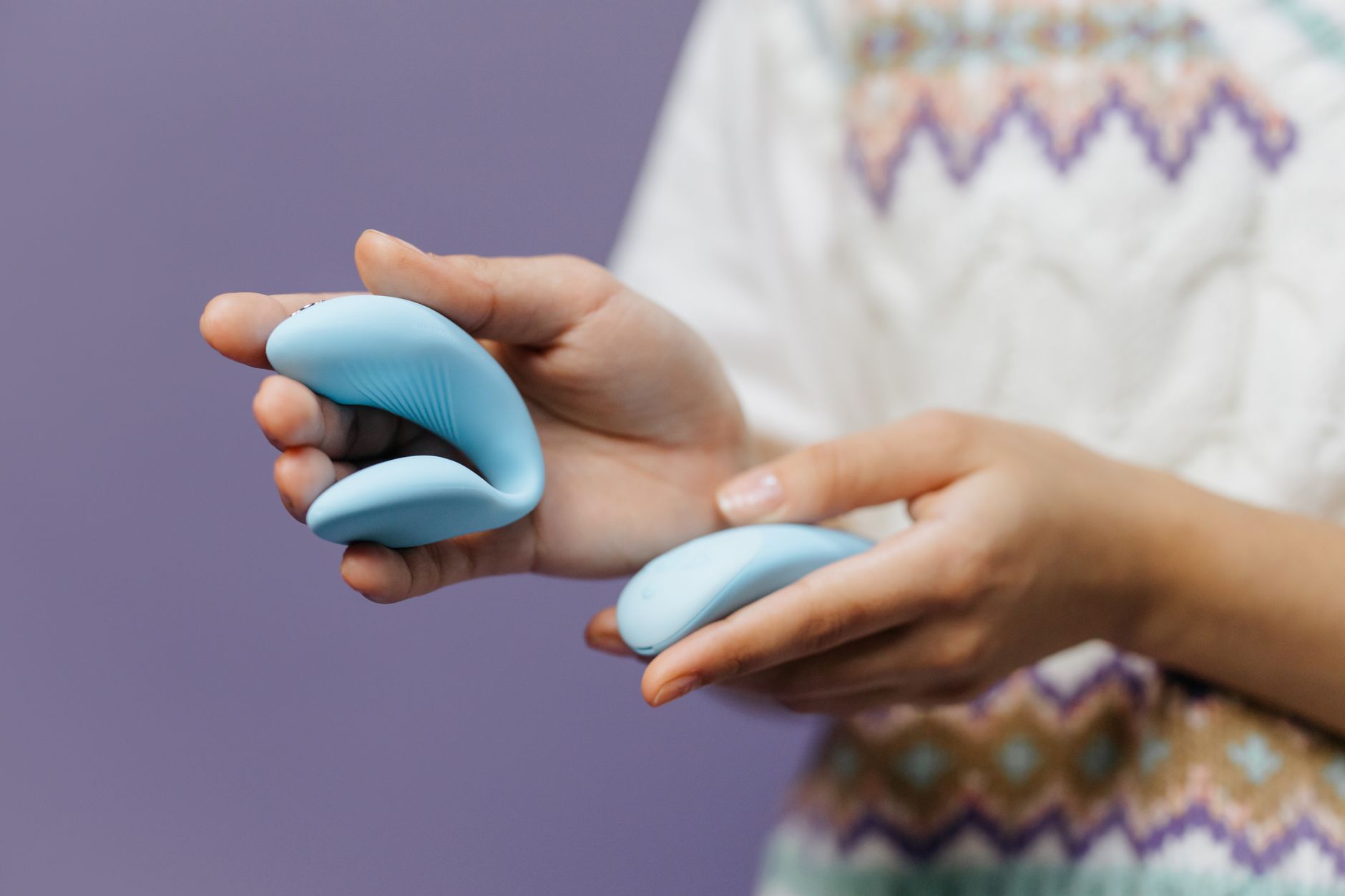 Hands holding a sleek blue lemon clitoral vibrator against a purple background, representing pleasure recovery and reconnection.