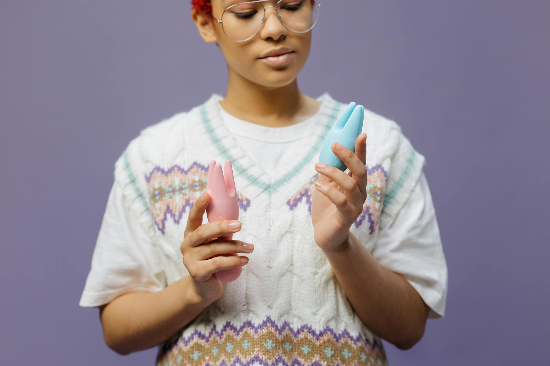 Woman holding blue and pink lemon clitoral vibrators in a thoughtful, deliberate pose