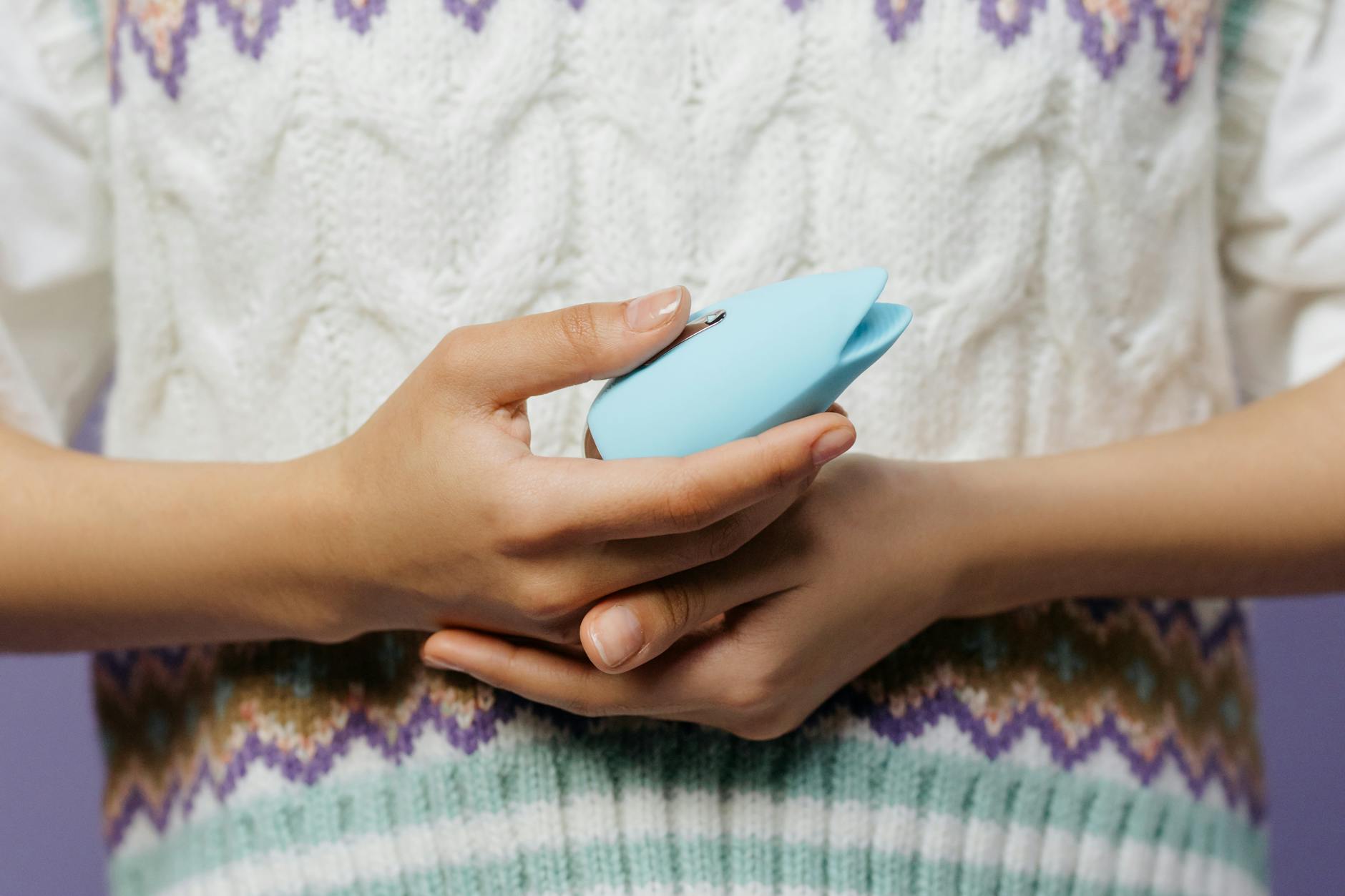 Close-up of hands holding a personal massager against a knitted sweater, representing comfort and solo pleasure.