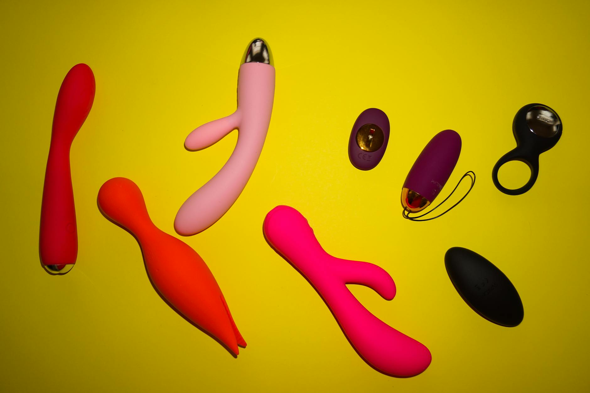 Colorful clitoral vibrators and lemon sex toys arranged on a bright yellow surface, showcasing various designs and textures.