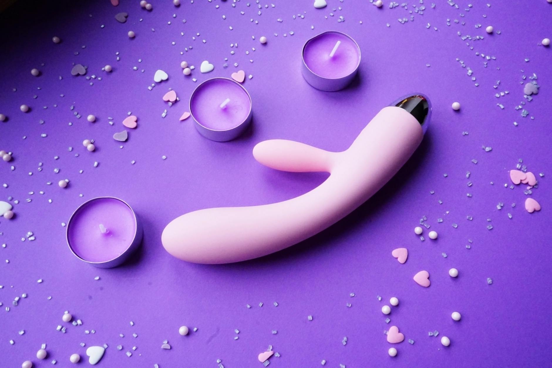 Pink vibrator on a purple background with heart confetti and candles for intimate pleasure